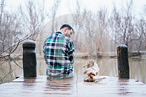 Smiling Hispanic man wearing flannel with Cavalier King Charles spaniel on a wooden dock in lake