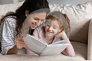 Smiling Hispanic mom and daughter reading book together