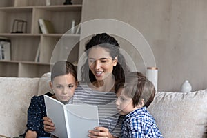 Smiling Hispanic mother reading book to little son and daughter