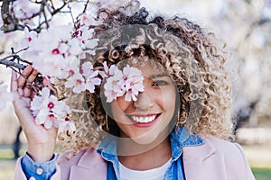 Smiling hispanic woman with eyes closed in park enjoying sunny day. Spring flowers background
