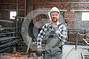 Smiling and holding wrench. Factory male worker in uniform is indoors