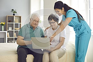 Home care nurse teaching her happy senior patients to use modern laptop computer photo