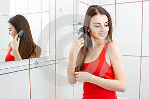Smiling hot girl combing her hair in the bathroom