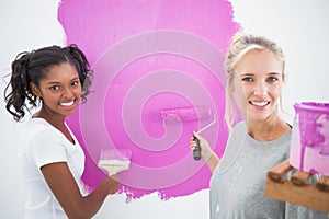 Smiling housemates painting wall pink