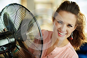 Smiling housewife cooling down using electric metallic fan