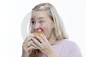 Smiling hungry teenage girl takes a bite of hamburger. Delicious and popular fast food. A cute blonde with freckles in a pink