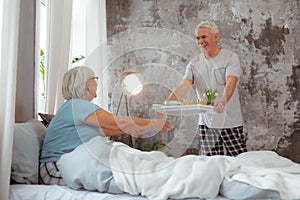 Smiling husband bringing breakfast to the bed of his wife.