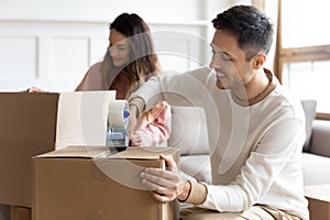 Smiling husband sealing box with adhesive tape, moving day