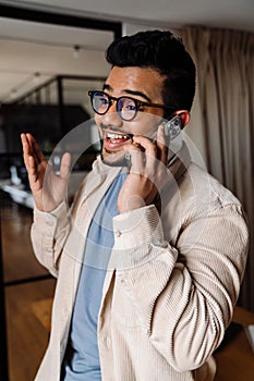 Smiling indian business man talking on mobile phone while standing in office