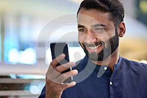 Smiling indian business man using smartphone looking at cellphone.