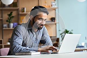 Smiling indian business man working studying on laptop computer at home office.