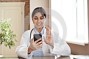 Smiling indian doctor video conference call patient in online mobile phone app.