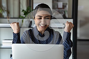Smiling Indian female employee read good news on laptop