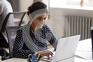 Smiling Indian female employee using laptop at workplace