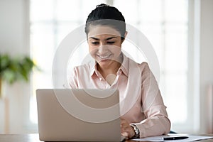 Smiling indian female employee work at laptop