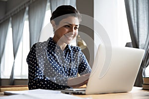 Smiling indian girl student professional typing on laptop at table