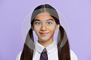 Smiling indian kid girl wear school uniform stand on lilac background, portrait.