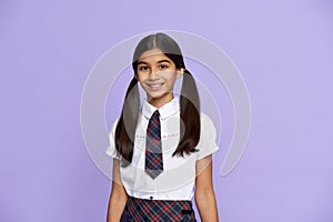 Smiling indian kid girl wear school uniform stand on lilac background, portrait.