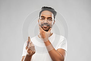 Smiling indian man applying grooming oil to beard