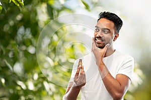 Smiling indian man applying grooming oil to beard