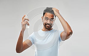 Smiling indian man applying hair spray over gray