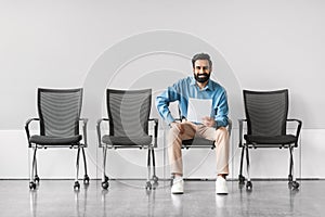 Smiling indian man sitting with document in a row of chairs