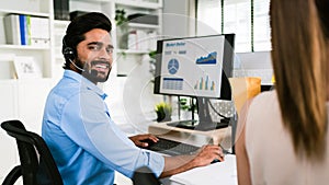 A smiling Indian man working as customer support operator with a headset in a call center. Portrait of sales agent sitting at desk