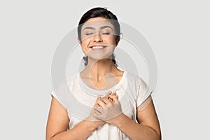 Smiling indian millennial girl standing with folded hands near heart.