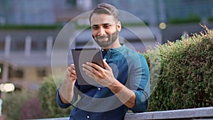 Smiling indian professional business man using digital tablet in city park.