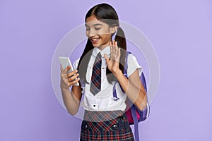 Smiling indian school girl video calling on mobile phone isolated on background.