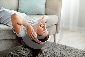 Smiling Indian teen girl in headphones listening to music or audio book, lying on sofa at home, copy space