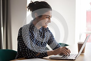 Smiling indian woman busy working on laptop in office
