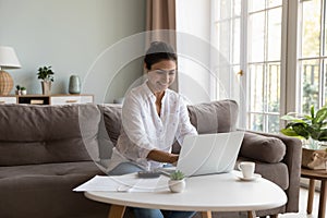 Smiling Indian woman paying bills through e-bank app use laptop