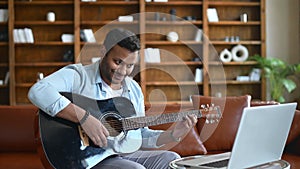 Smiling Indian young man learning how to play guitar online,