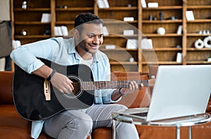 Smiling indian young man learning how to play guitar online