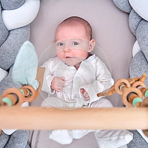 Smiling infant baby boy playing with a wooden mobile suspended above the crib. Happy child playing in bed with toys