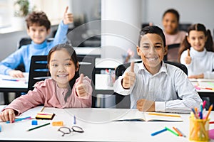 Smiling international schoolchildren showing thumbs up gesture