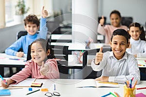 Smiling international schoolchildren showing thumbs up gesture