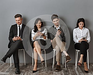 smiling interracial business people in formal wear using smartphones while waiting