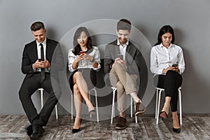 smiling interracial business people using smartphones while waiting