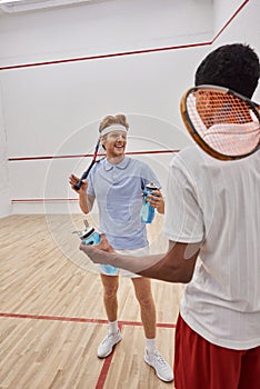 smiling interracial sportsmen with squash racquets