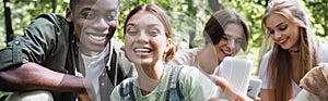Smiling interracial teenagers taking selfie near