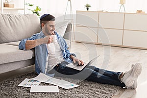 Smiling jewish man watching video on pc, drinking hot coffee