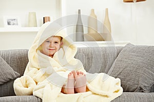 Smiling kid in bathrobe at home sofa bare feet