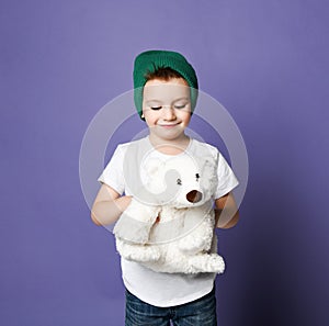 Smiling kid boy in green hat hugs his polar bear toy and looks at it with love. International day of polar bear concept
