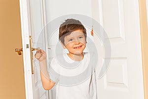Smiling kid boy opening the white door at home