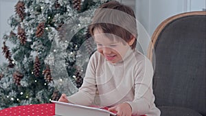 Smiling kid boy sitting on a chair and playing with tablet during Christmas time