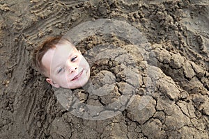 Smiling kid buried in sand on beach