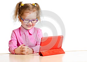 Smiling kid in glasses looking at mini tablet pc screen sitting