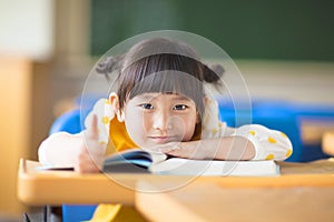 Smiling kid lie prone on a desk and thumb up